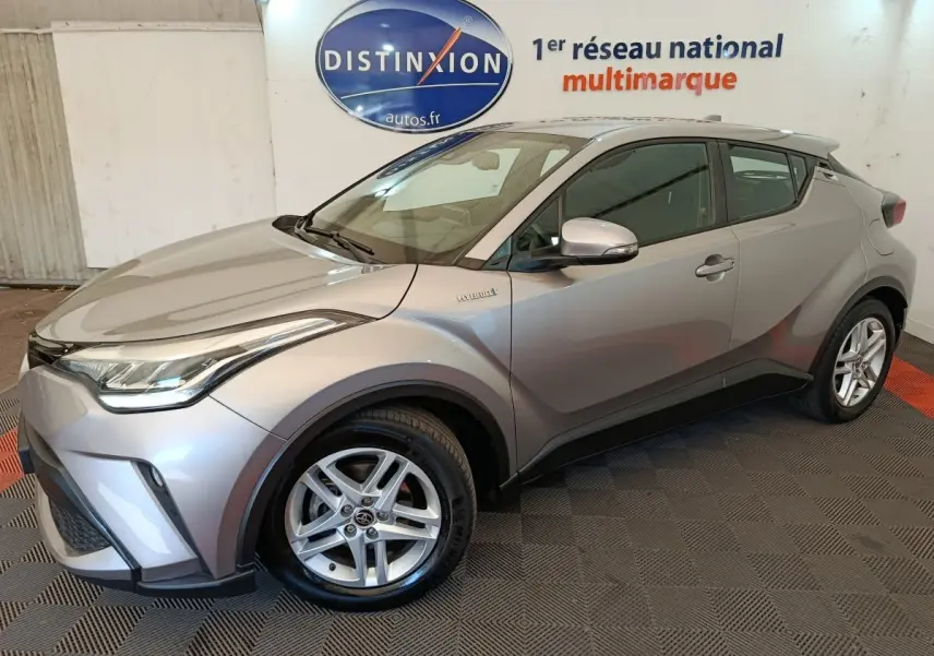 Vue 3/4 avant droit d’un Toyota C-HR 2.0 Hybride gris clair, avec jantes alliage et détails hybrides visibles sur l’aile.