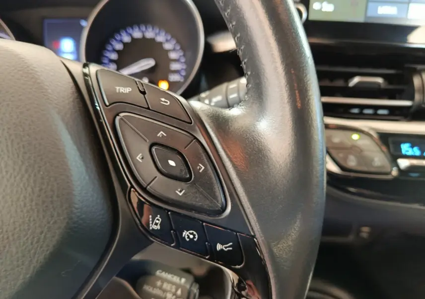 Gros plan sur le volant cuir du Toyota C-HR gris clair 2022, avec commandes multifonctions et tableau de bord en arrière-plan.
