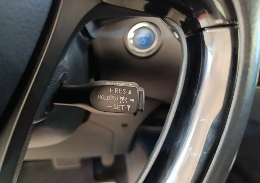 Gros plan sur la commande du régulateur de vitesse au volant d'un Toyota C-HR gris clair, intérieur noir.