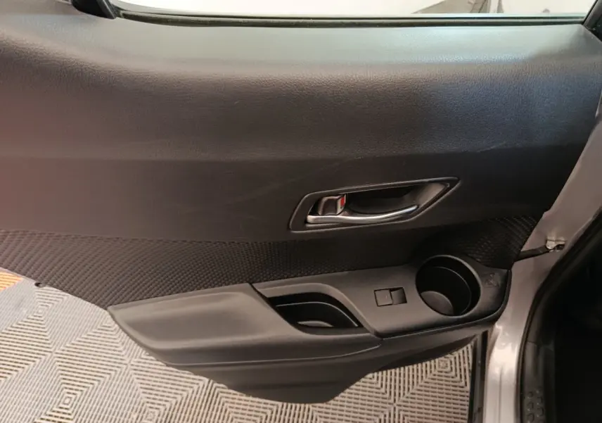 Vue intérieure côté gauche de la porte avant grise claire du Toyota C-HR 2.0 Hybride avec poignée et porte-gobelet.
