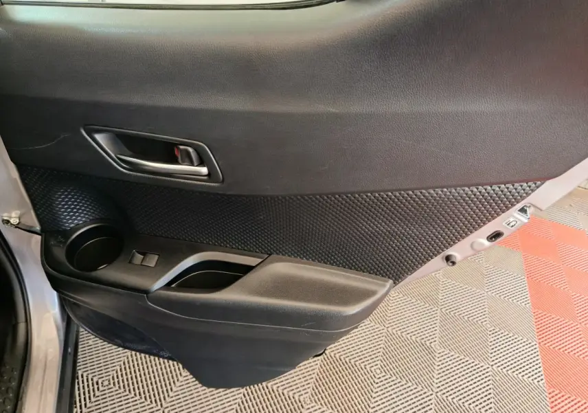 Gros plan sur la porte arrière gauche intérieure du Toyota C-HR gris clair, avec poignée et rangement intégré.