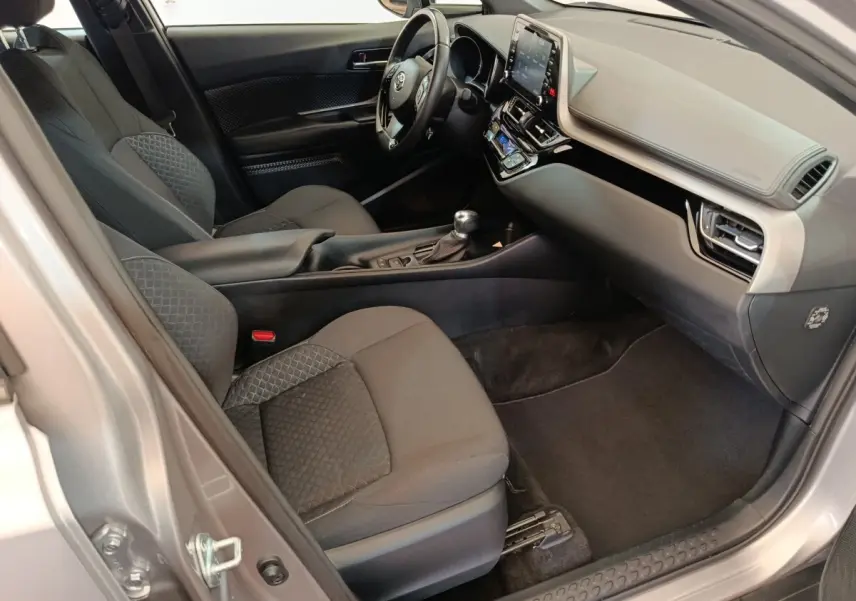 Vue intérieure côté passager du Toyota C-HR gris clair 2022, avec tableau de bord moderne et sièges tissu noirs.