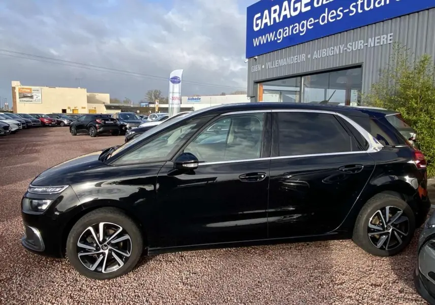 Profil côté gauche d'une Citroën C4 Spacetourer noire avec jantes alliage bi-ton 17 pouces sur parking extérieur.