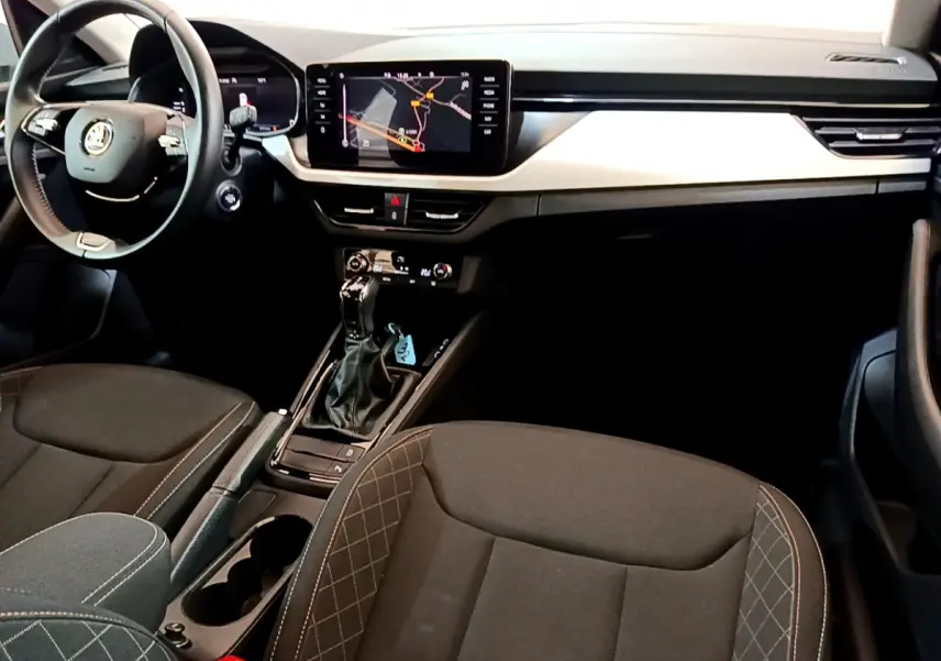 Intérieur du Skoda Kamiq 2022 vu côté conducteur, tableau de bord noir avec écran tactile et sièges tissu gris foncé.