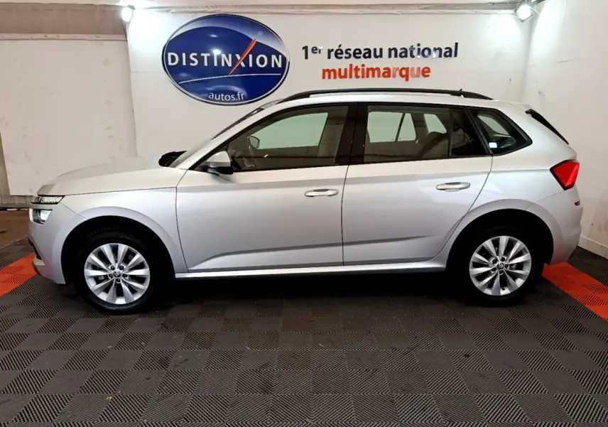 Vue de profil côté gauche d'un Skoda Kamiq gris clair 2022 dans un showroom avec logo Distinxion en arrière-plan.