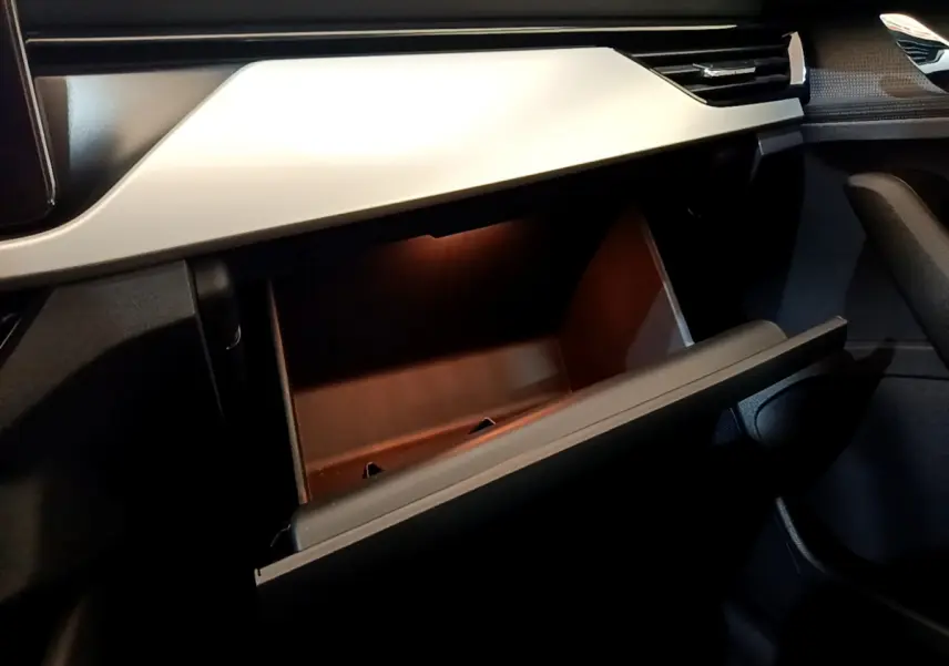 Intérieur du Skoda Kamiq 2022, vue sur la boîte à gants ouverte avec éclairage intérieur et tableau de bord gris clair.