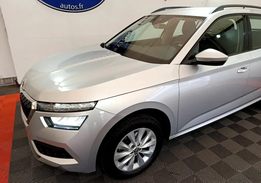 Vue 3/4 avant droit d'un Skoda Kamiq gris clair avec phares LED et jantes alliage en intérieur showroom.