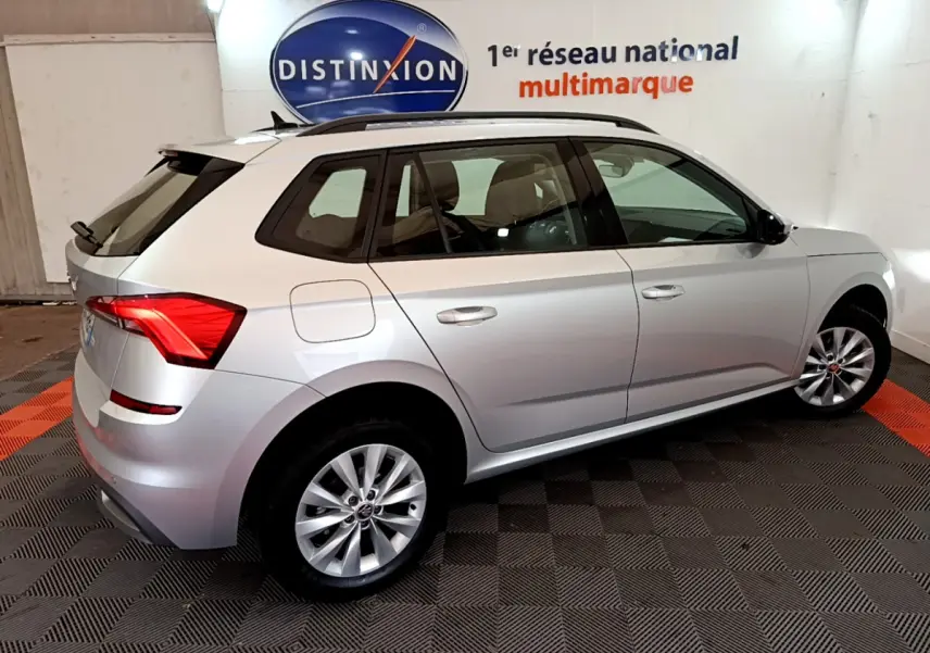 Vue 3/4 arrière droite d'un Skoda Kamiq gris clair 2022 avec jantes alliage et barres de toit noires.