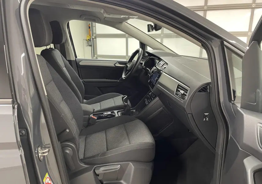 Vue intérieure côté conducteur du Volkswagen Touran gris Dauphin 2024, montrant sièges et tableau de bord modernes.