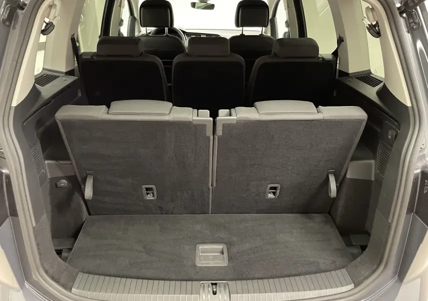 Coffre ouvert d'un Volkswagen Touran gris dauphin 2024, vue arrière montrant la troisième rangée de sièges relevée.