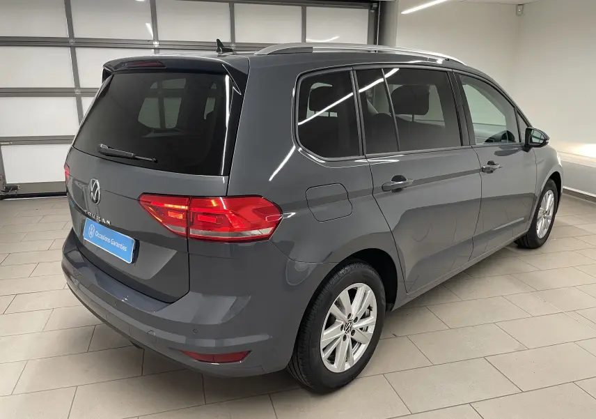 Volkswagen Touran gris dauphin vu en 3/4 arrière droit dans un garage, hayon et vitres teintées visibles.