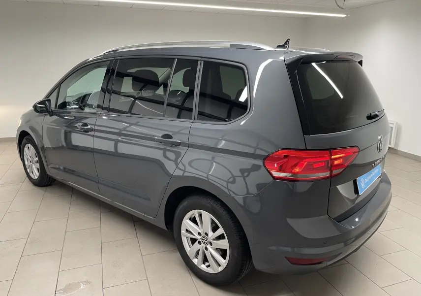 Volkswagen Touran 2024 gris dauphin vu en 3/4 arrière droit dans un intérieur lumineux avec hayon fermé.