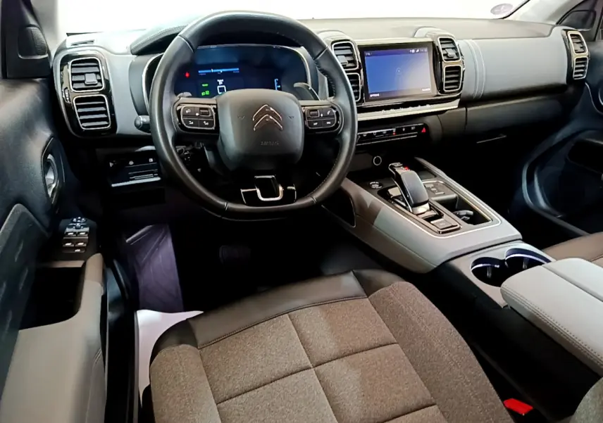 Vue intérieure avant du Citroën C5 Aircross Hybrid gris clair, volant cuir, écran tactile et console centrale moderne.