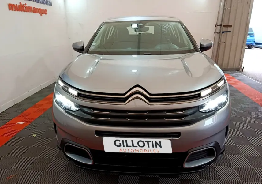 Vue frontale d'un Citroën C5 Aircross gris clair avec phares LED allumés dans un showroom fermé.