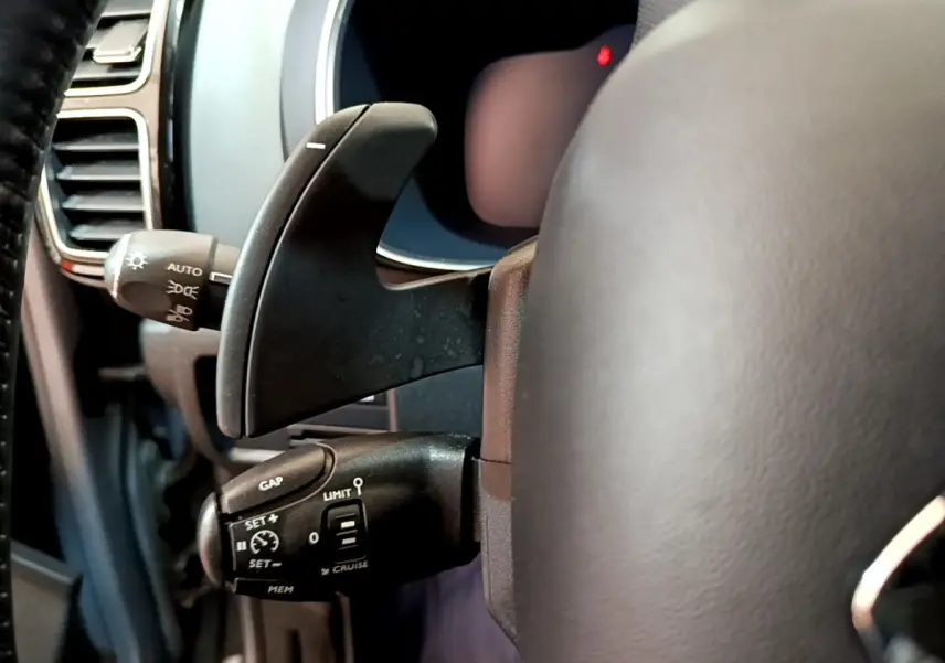 Gros plan sur la commande de régulateur de vitesse à gauche du volant cuir du Citroën C5 Aircross Hybrid 225 gris clair.