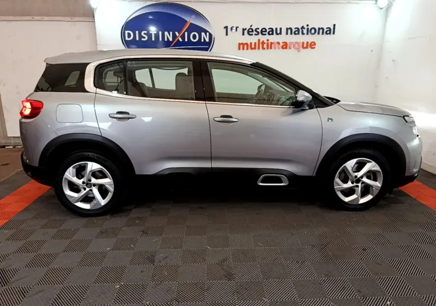 Profil côté droit du Citroën C5 Aircross Hybrid gris clair avec jantes alliage et feux arrière allumés en intérieur showroom.