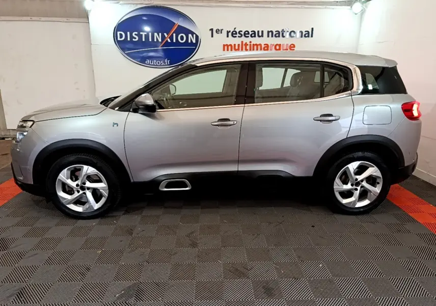 Profil côté gauche d'un Citroën C5 Aircross Hybrid gris clair en intérieur avec jantes alliage et logo hybride visible.