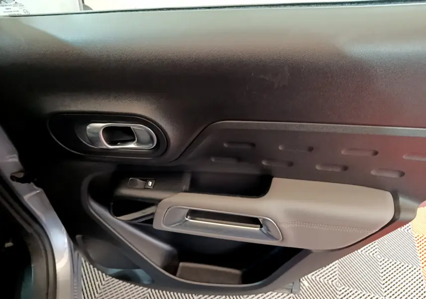 Vue rapprochée de la porte côté gauche du Citroën C5 Aircross Hybrid gris clair, avec poignée intérieure chromée et accoudoir beige.