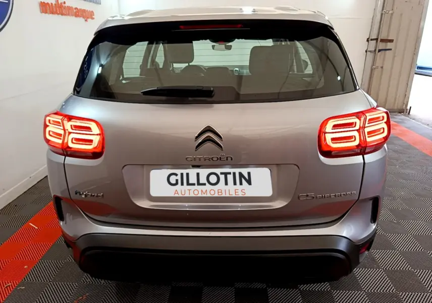 Vue arrière d'un Citroën C5 Aircross Hybrid gris clair avec feux arrière LED allumés en intérieur showroom.