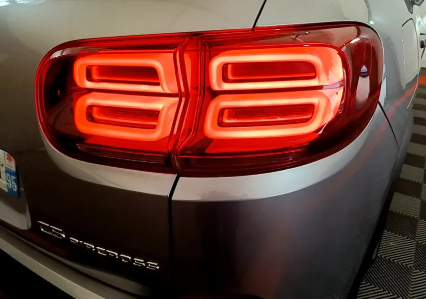 Feu arrière droit allumé sur Citroën C5 Aircross gris clair, détail du logo et de la carrosserie arrière.