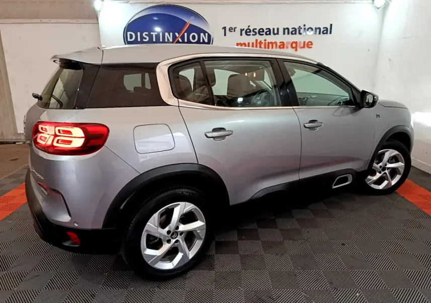 Vue 3/4 arrière droite d'un Citroën C5 Aircross Hybrid gris clair avec feux arrière LED allumés en intérieur showroom.