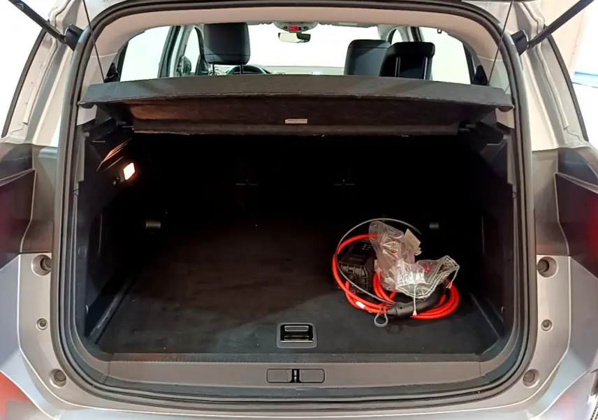 Coffre ouvert vu de l'arrière d'un Citroën C5 Aircross gris clair avec câble de recharge hybride visible à droite.