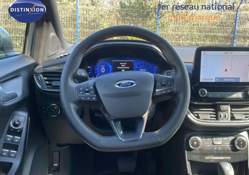 Vue intérieure frontale du tableau de bord et volant noir perforé de la Ford Puma gris Solar Metal 2023 avec écran tactile et commandes intégrées.