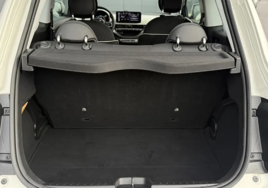 Vue arrière du coffre ouvert d'une FIAT 500 électrique blanche, montrant l'espace de chargement et les sièges noirs.