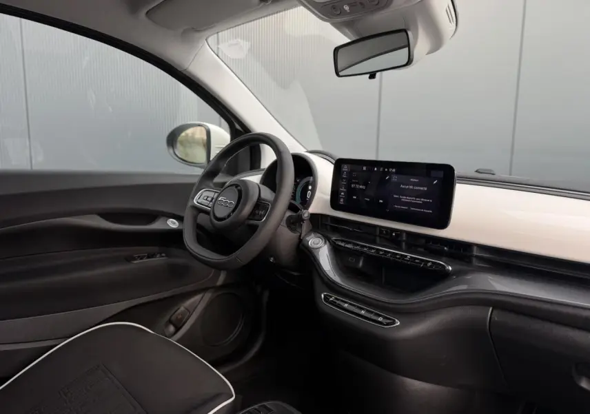 Vue intérieure côté conducteur de la Fiat 500 électrique 2024 avec tableau de bord blanc et écran tactile central.