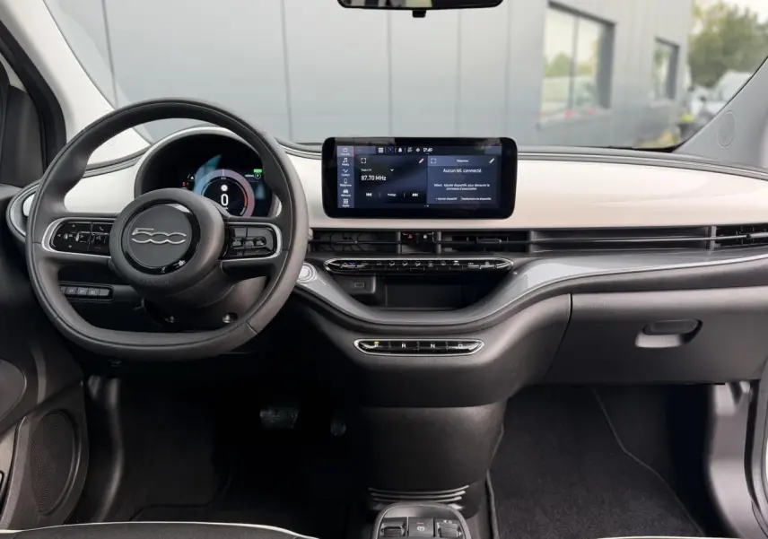 Vue intérieure avant de la Fiat 500 électrique 2024 avec tableau de bord blanc et écran tactile central large.