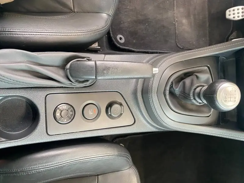 Vue plongeante sur la console centrale noire du Peugeot RCZ 1.6 THP 2010, montrant levier de vitesse manuel et frein à main cuir.