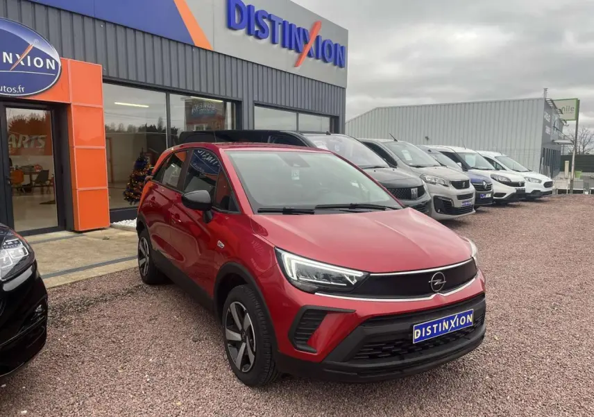 Opel Crossland rouge métallisé en 3/4 avant droit, avec feux LED et calandre noire, stationné devant un concessionnaire.