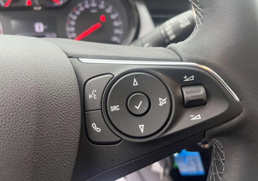 Gros plan sur les commandes au volant noir de l'Opel Crossland rouge, avec boutons de volume et appels téléphoniques.
