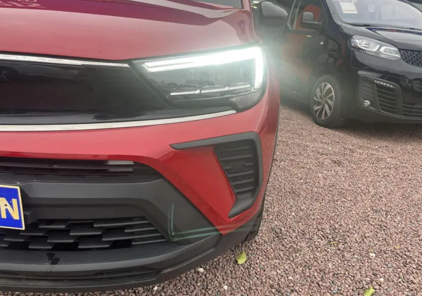 Gros plan sur l'avant droit rouge d'un Opel Crossland 2022 avec phare LED allumé et calandre noire.