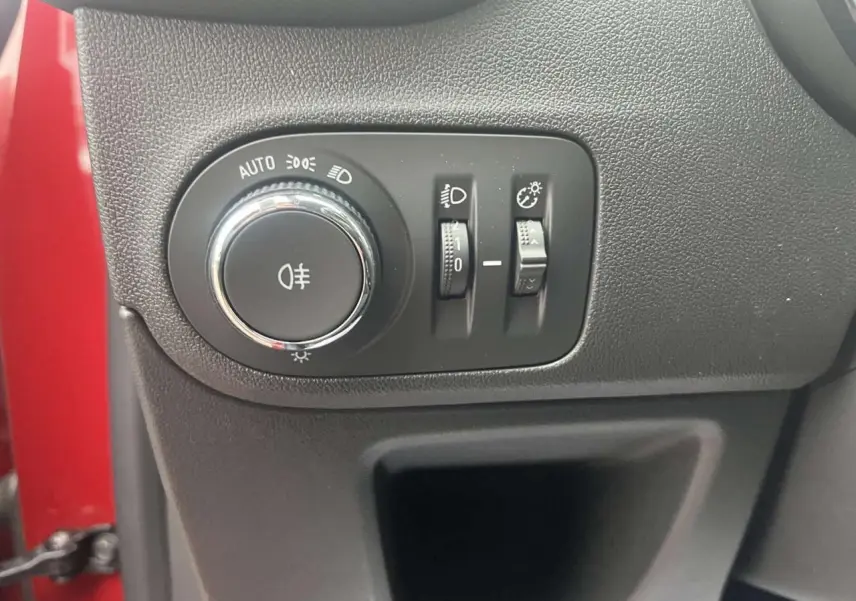 Gros plan sur le panneau de commande des phares à gauche du volant, avec la carrosserie rouge visible en arrière-plan.