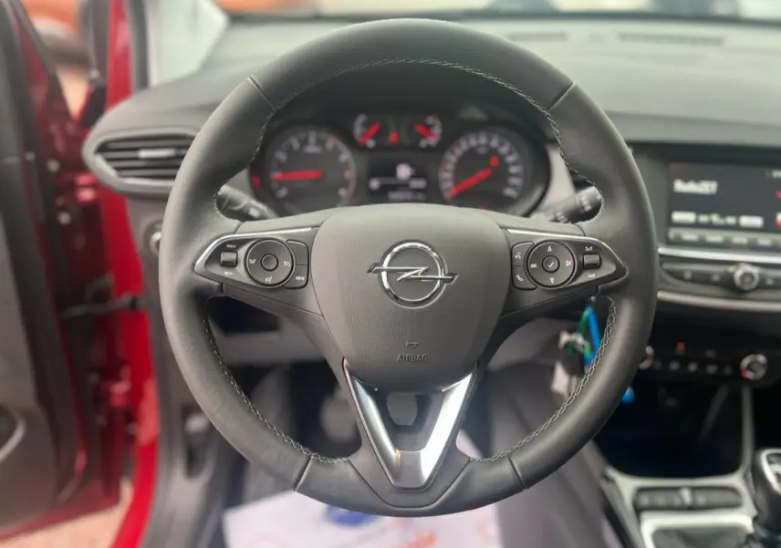 Vue rapprochée du volant noir de l’Opel Crossland rouge 2022, avec tableau de bord et écran tactile en arrière-plan.