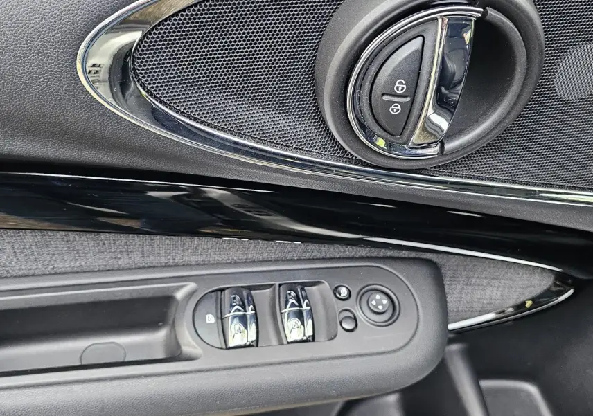 Poignée intérieure côté gauche de la MINI Cooper S Clubman 2022 avec commandes de vitres et verrouillage sur garniture noire et tissu gris.