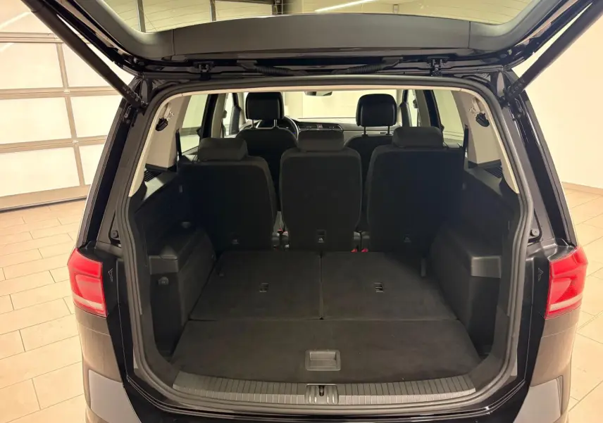 Coffre ouvert d'un Volkswagen Touran noir intense nacré, vue arrière montrant les sièges arrière et l'espace de chargement.
