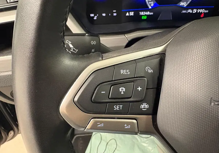 Gros plan sur les commandes au volant du Volkswagen Touran 2024 noir intense nacré, affichage digital en arrière-plan.