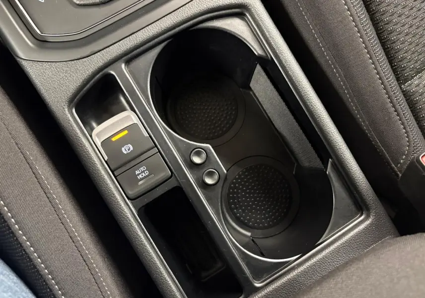 Gros plan sur la console centrale noire avec porte-gobelets et bouton frein à main électrique du Volkswagen Touran 2024.