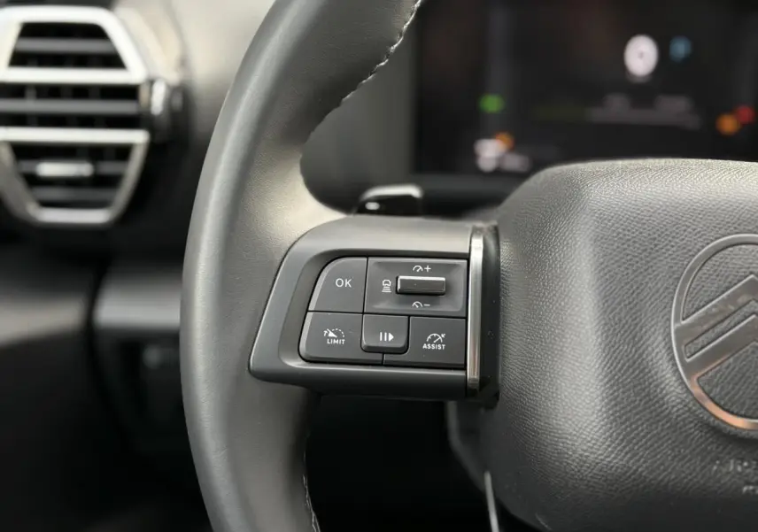 Gros plan sur les commandes au volant côté gauche du Citroën C4 Hybrid gris Mercury, avec aérateur en arrière-plan.