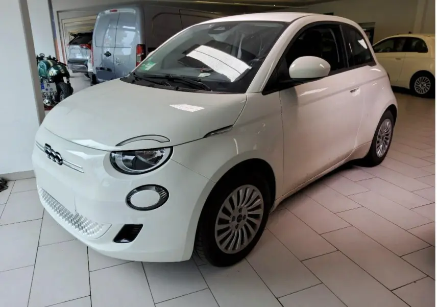 Vue 3/4 avant d'une FIAT 500 électrique blanche, avec logo distinctif et jantes multibranches visibles.