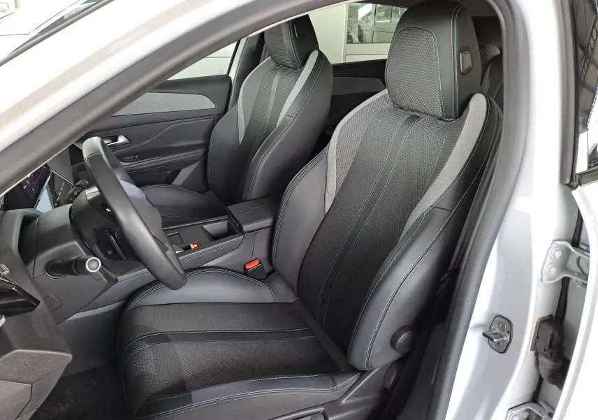 Vue intérieure côté conducteur de la Peugeot 308 2024 blanc Okenite, sièges noirs avec surpiqûres bleues et tissu mixte.