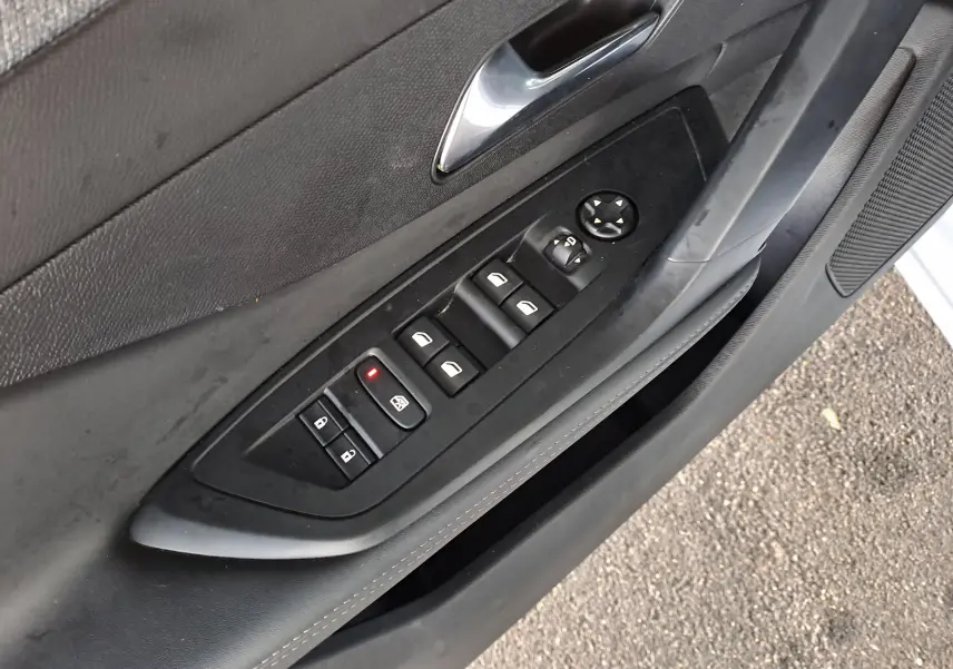 Panneau de commande des vitres et rétroviseurs côté gauche intérieur noir de la Peugeot 308 blanche 2024.