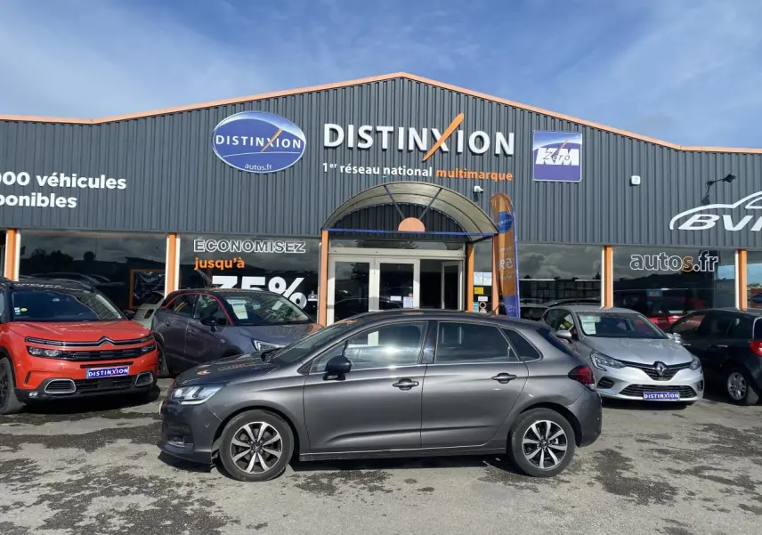 Profil côté gauche d'une Citroën C4 gris platinium 2017 garée devant un concessionnaire multimarque.