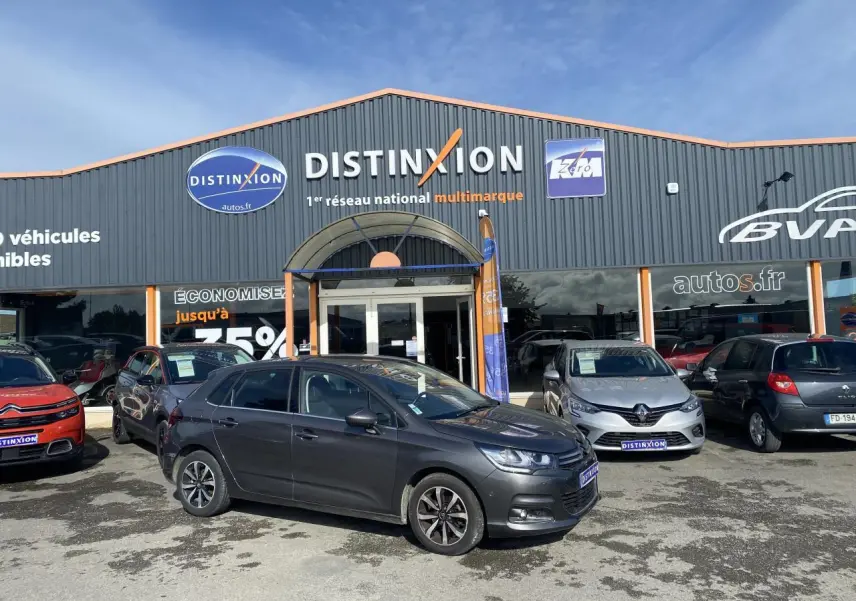 Citroën C4 gris platinium vue de profil côté gauche, stationnée devant un concessionnaire Distinxion.