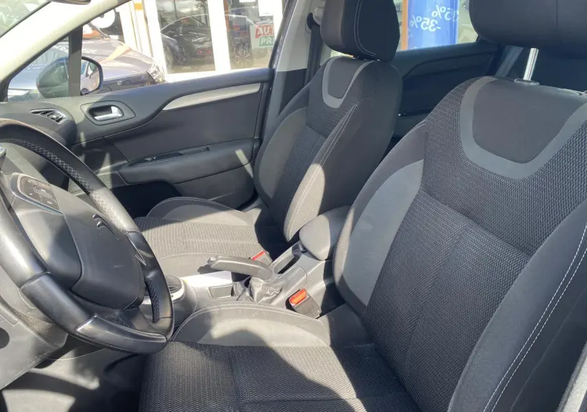 Vue intérieure côté conducteur et passager avant d'une Citroën C4 2017 avec sièges tissu gris et volant multifonction.