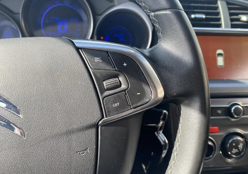 Gros plan sur le volant en cuir noir de la Citroën C4 2017 avec commandes audio et tableau de bord lumineux bleu.