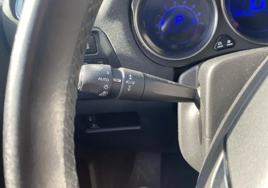 Gros plan sur la manette des feux et le tableau de bord numérique bleu du Citroën C4 gris platinium, côté gauche du volant.