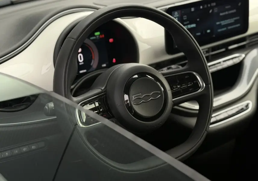 Vue intérieure avant du tableau de bord blanc et noir de la Fiat 500 électrique 2024 avec écran tactile central et volant multifonction.
